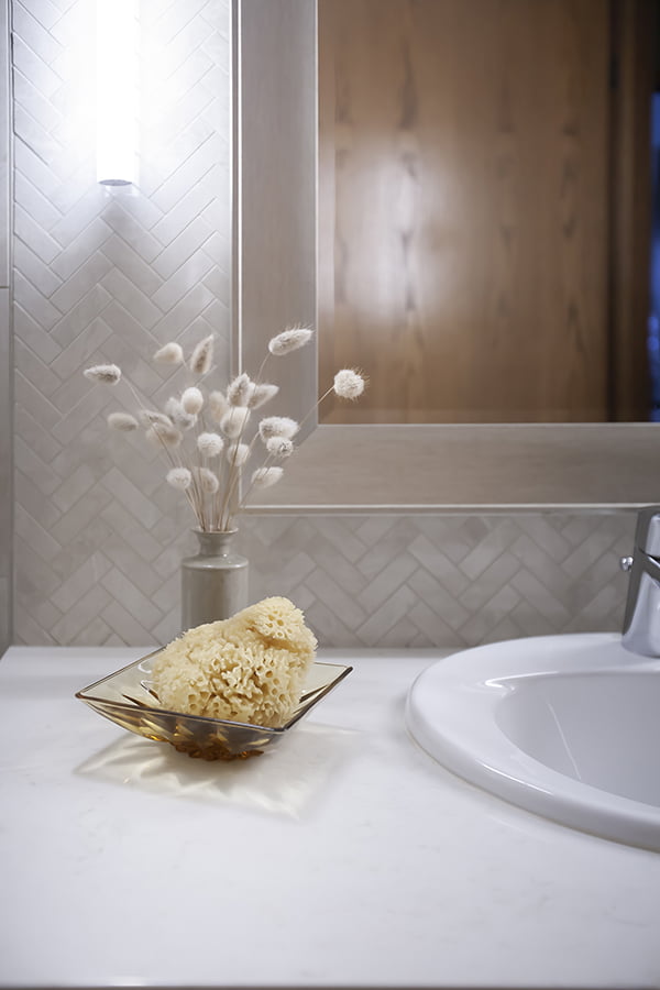 custom bathroom with small herringbone style tile backsplash and stone countertops